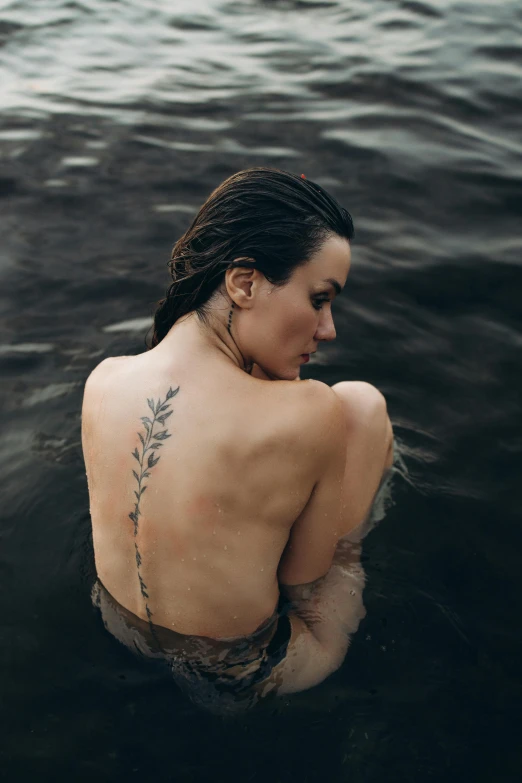 woman with leaf tattoo sitting in water looking off to side