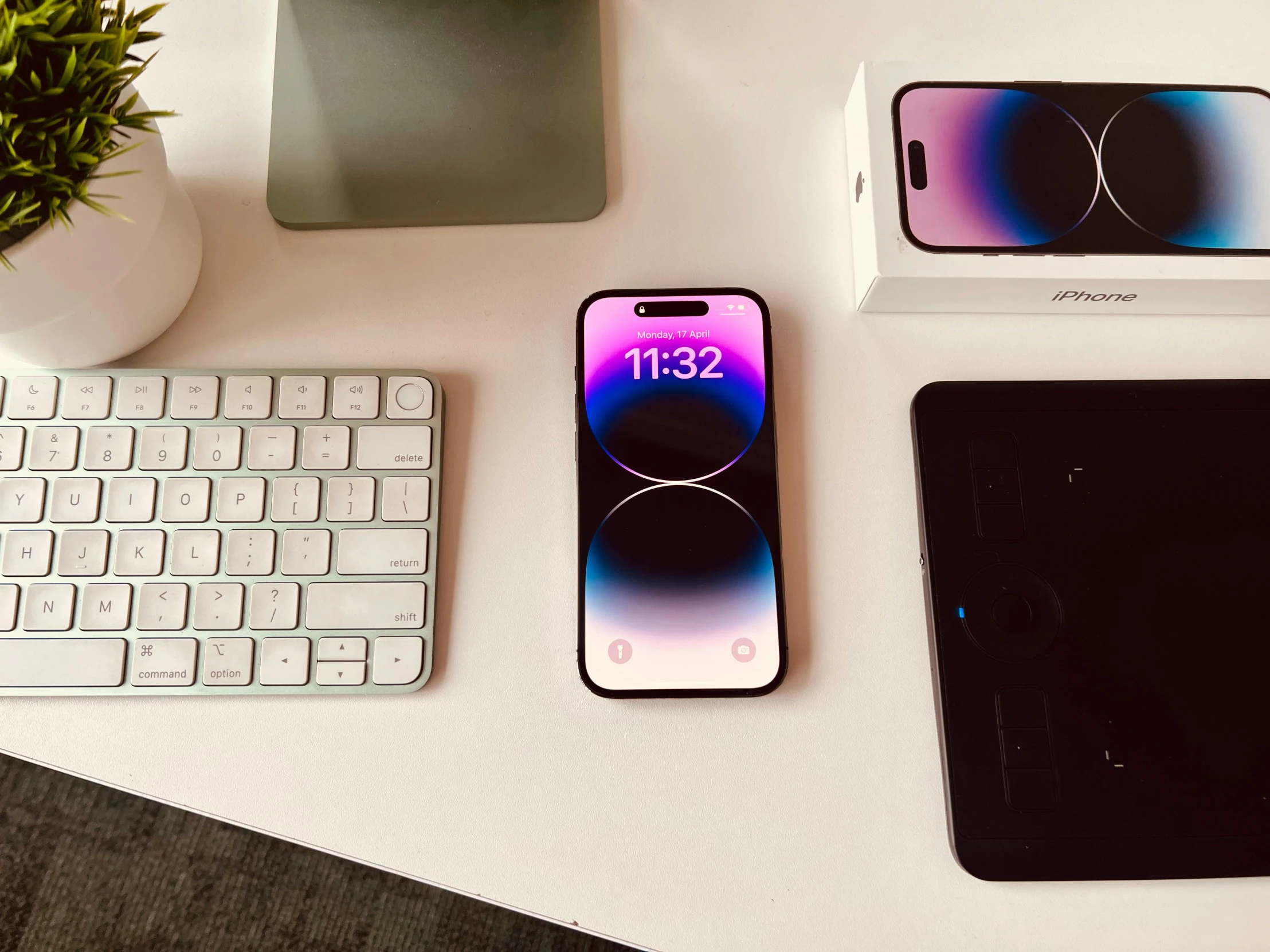 a phone is displayed on a desk next to a keyboard and a plant