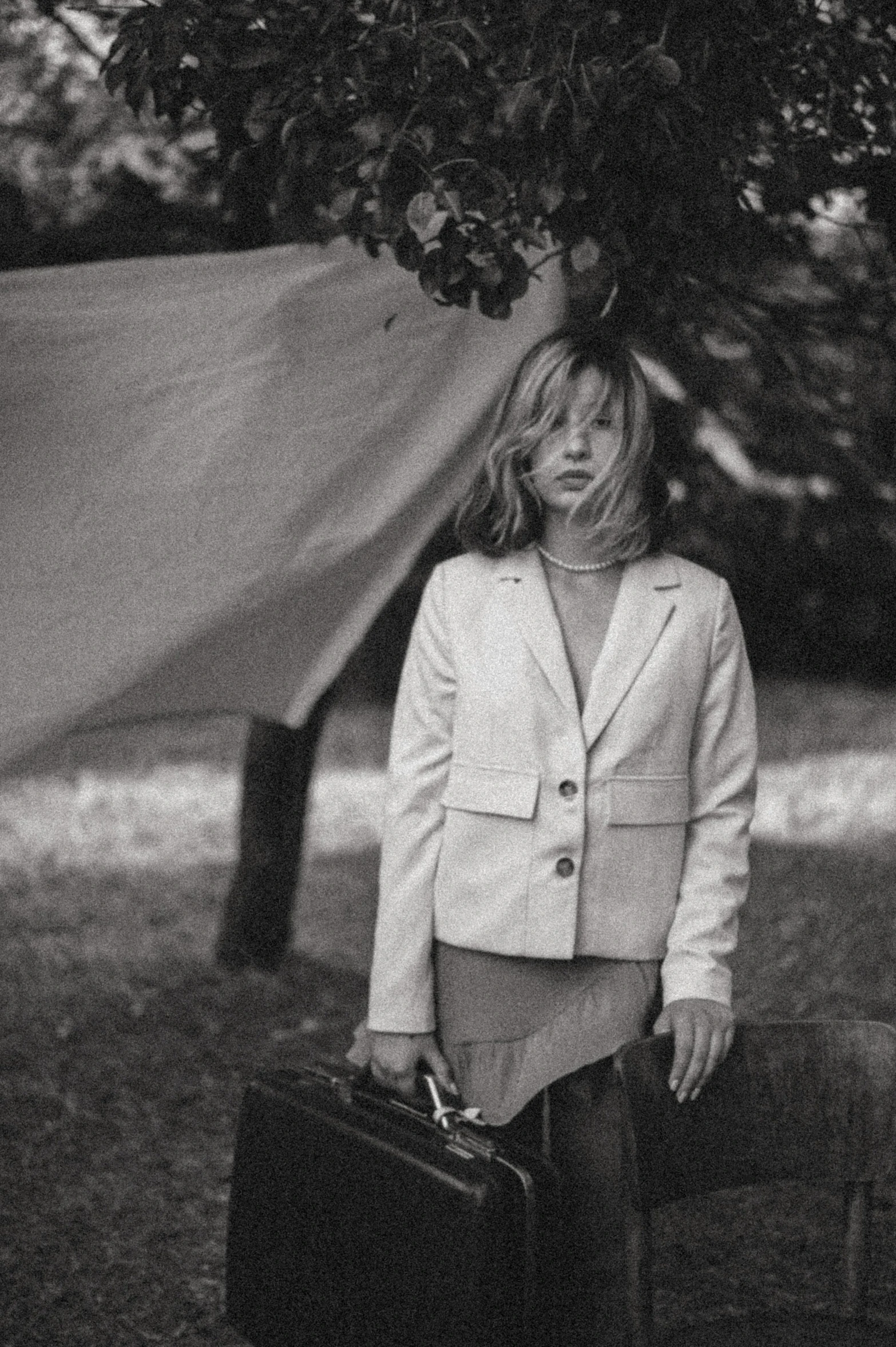 a woman standing under a tree with a suit case