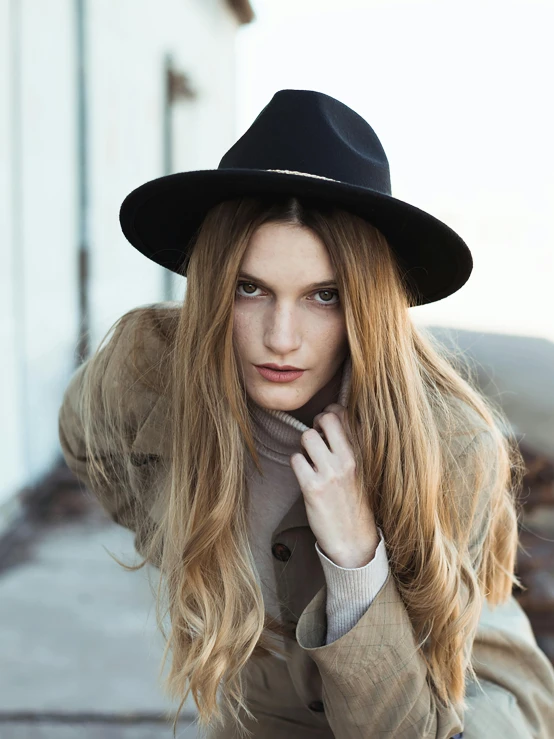 a woman in a coat and black hat sitting on the curb