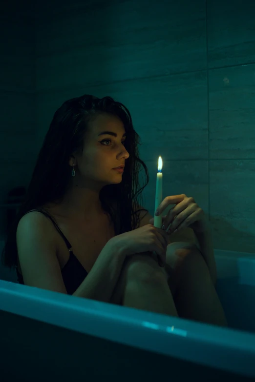 a woman sits in a bath tub holding a candle