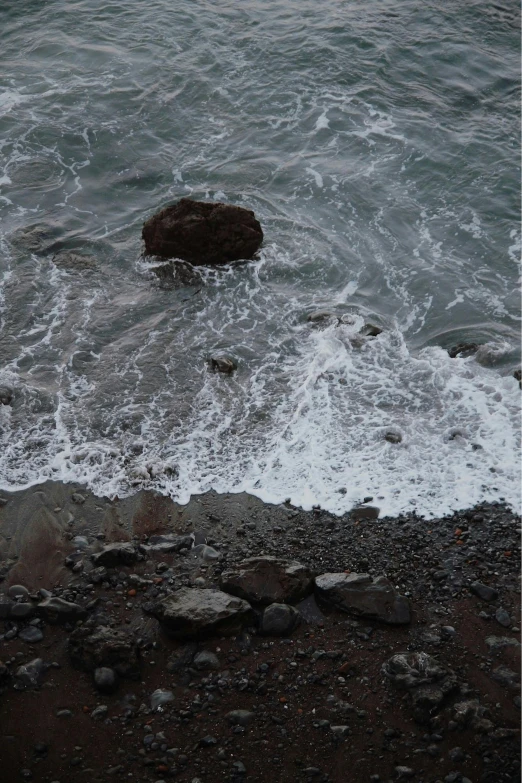 rocks are seen on the beach while waves come in