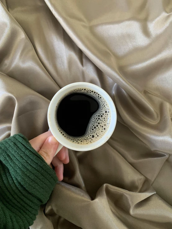 a person's hand holding a cup of coffee on a bed