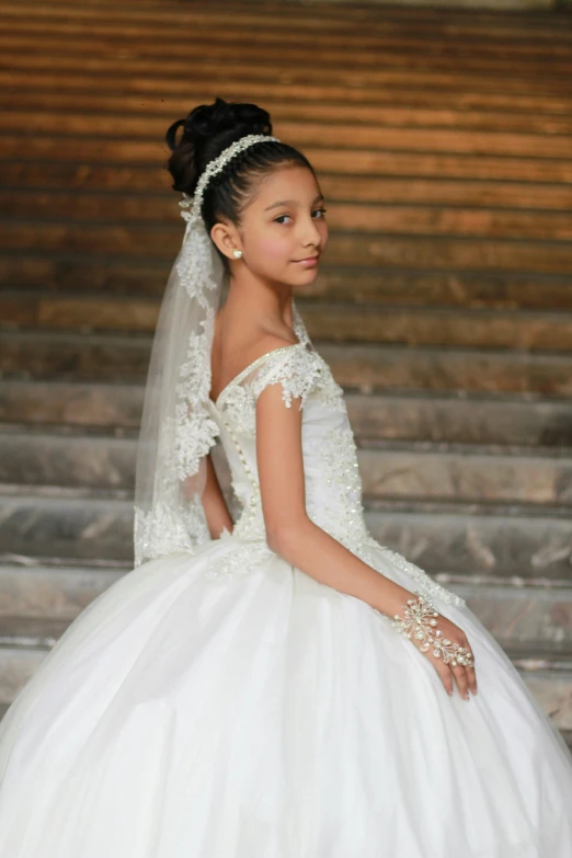 a small girl wearing a wedding dress in front of some stairs