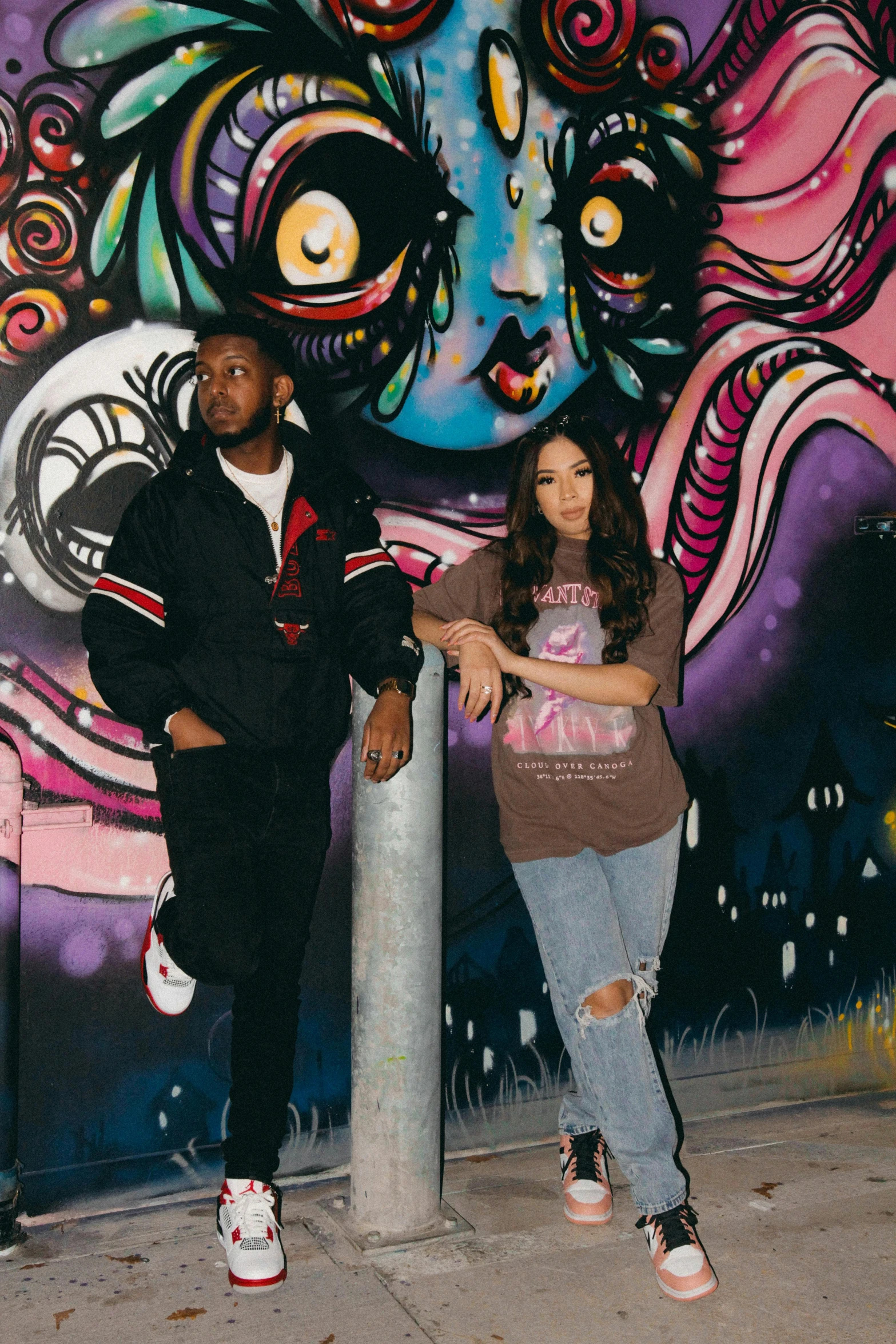 a young man and woman stand near a large colorful piece of art