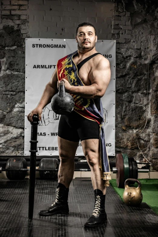 man posing shirtless with a kettle while wearing boxing trunks