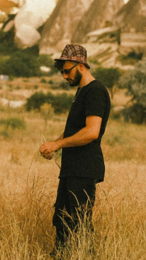 a man with a beard wearing a hat standing in tall grass
