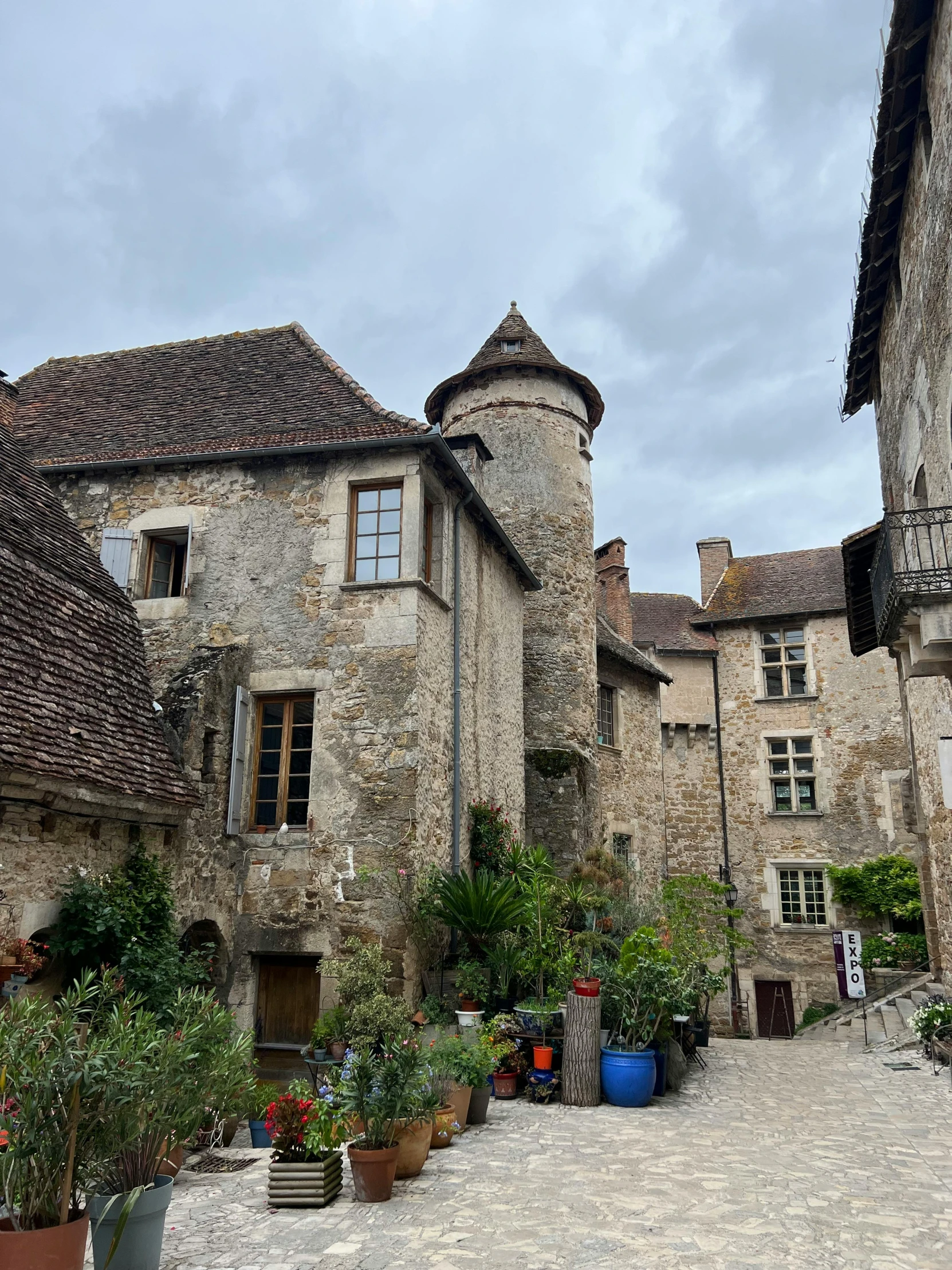 a cobblestone road lined with potted plants and large stone buildings