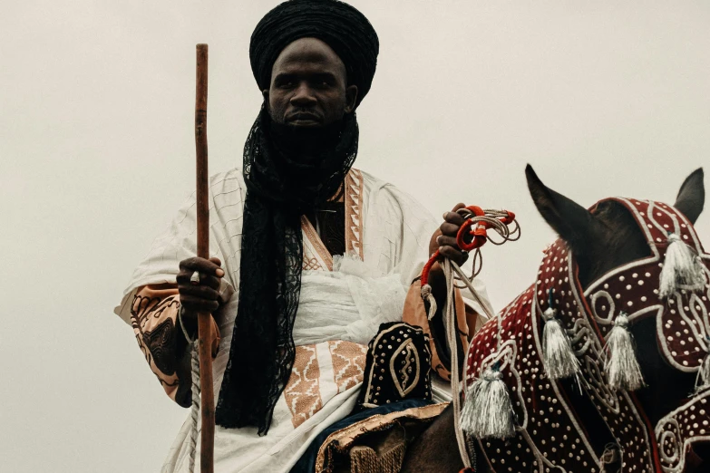 an african man riding a horse while holding a stick