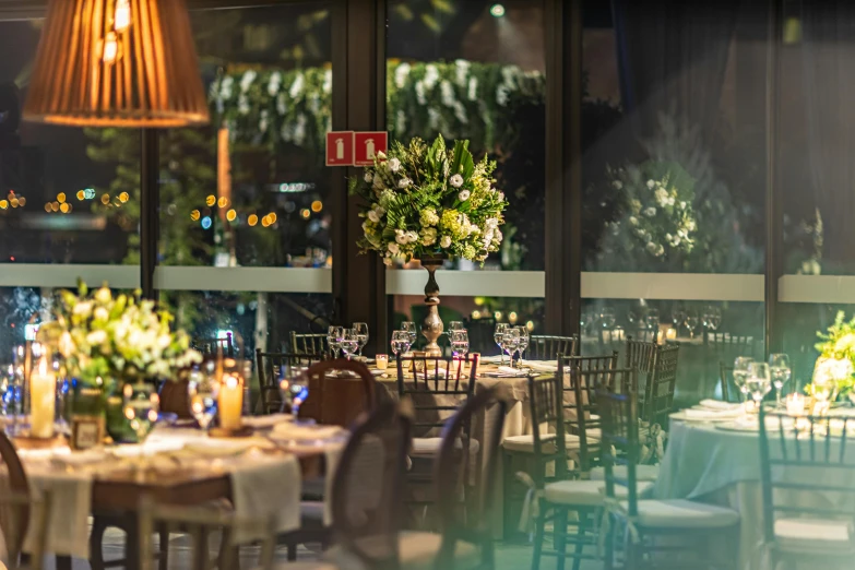 a restaurant filled with tables covered in white linens and topped with lots of green plants