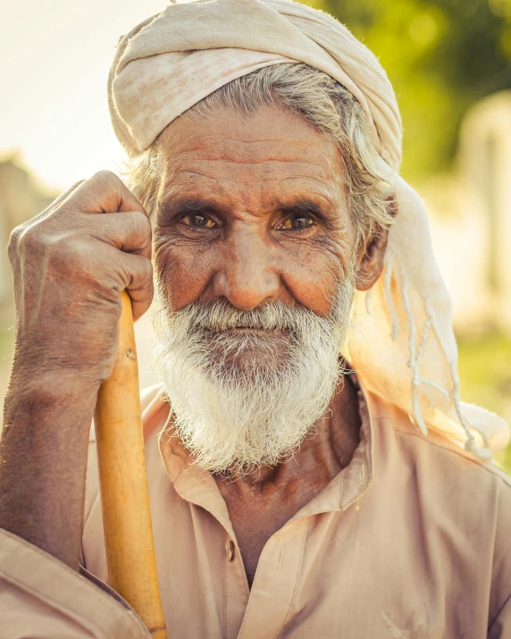 an older man holds a stick while wearing a turban