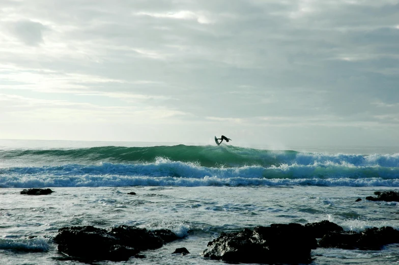 man on surfboard riding small wave in ocean with rocks