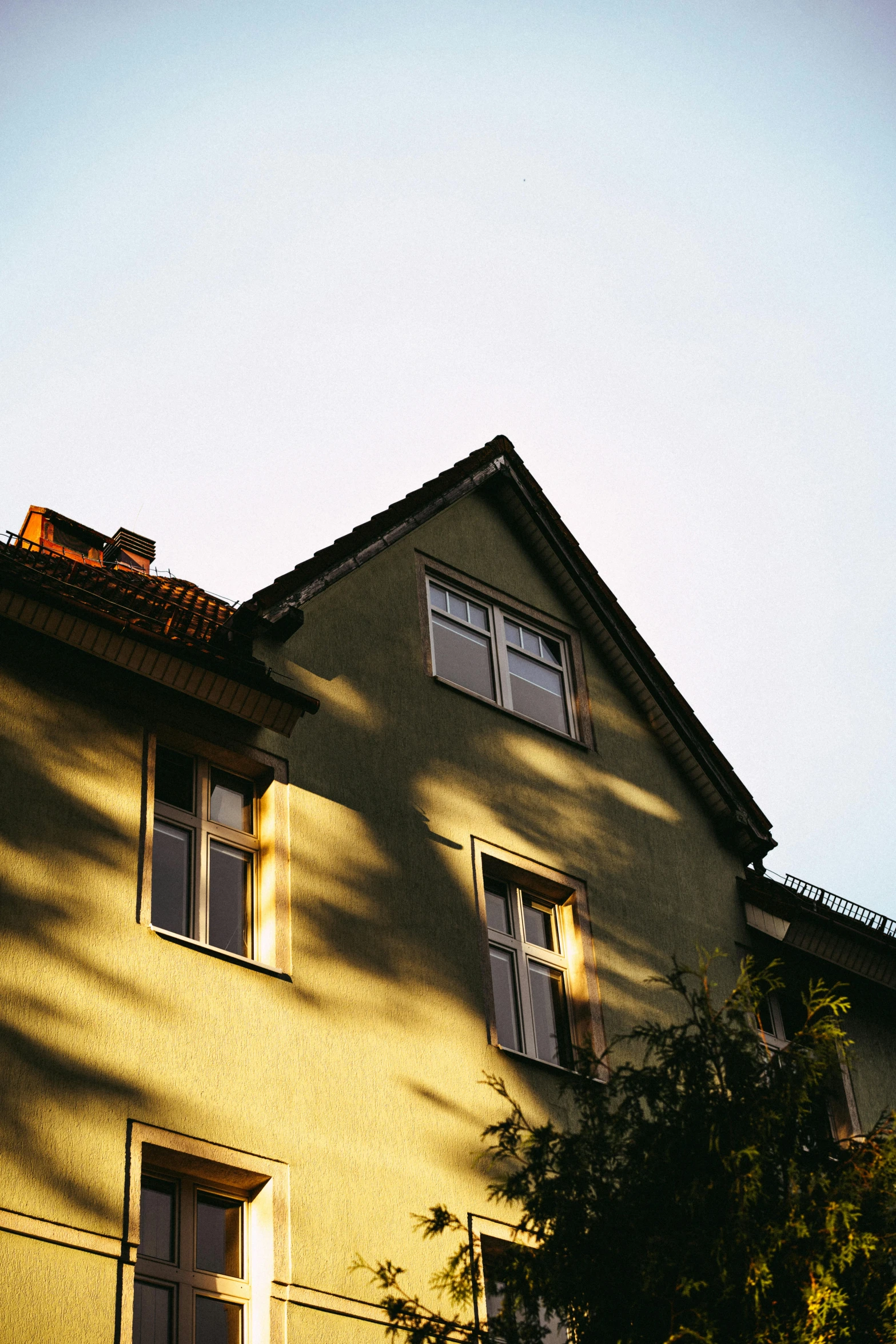 the corner of an older yellow house with trees