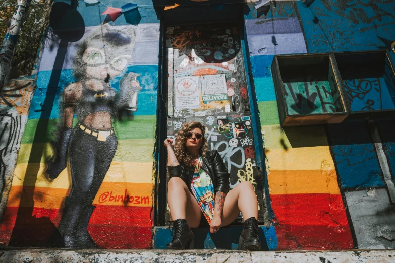 a person with sunglasses is sitting next to a wall painted with colorful images