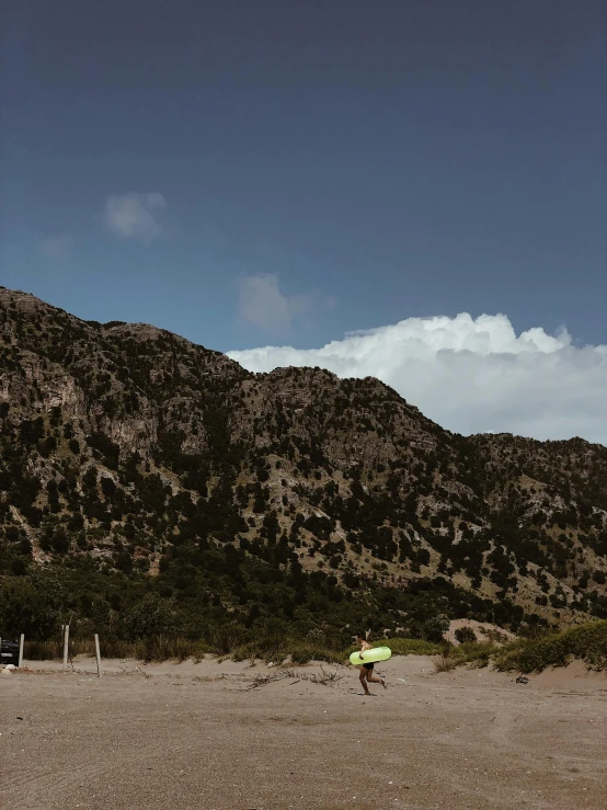 person running near the mountains carrying a green and yellow frisbee