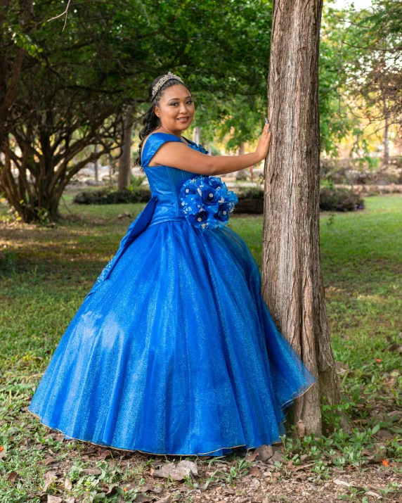 a woman dressed in a blue dress leaning against a tree