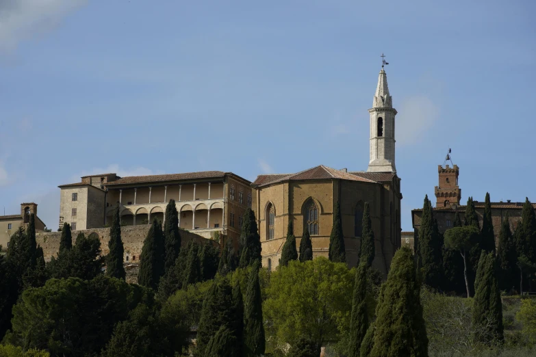 a clock tower above several old buildings, as seen through some trees