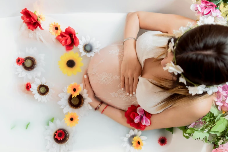 a pregnant woman with flowers around her, taking a bath