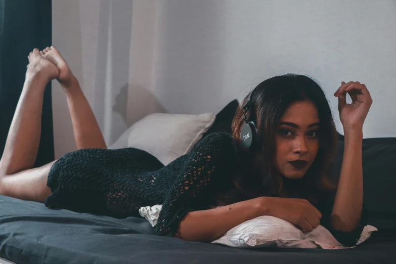 young woman laying down on bed listening to music