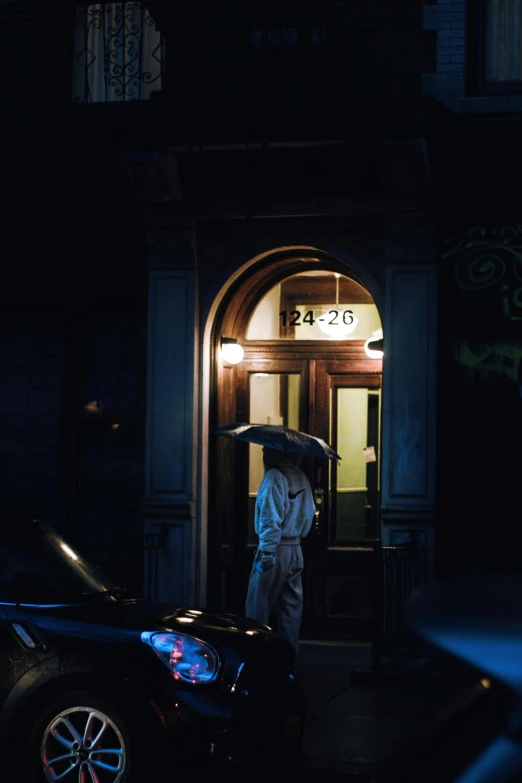 a person with an umbrella walking away from the dark door of a building