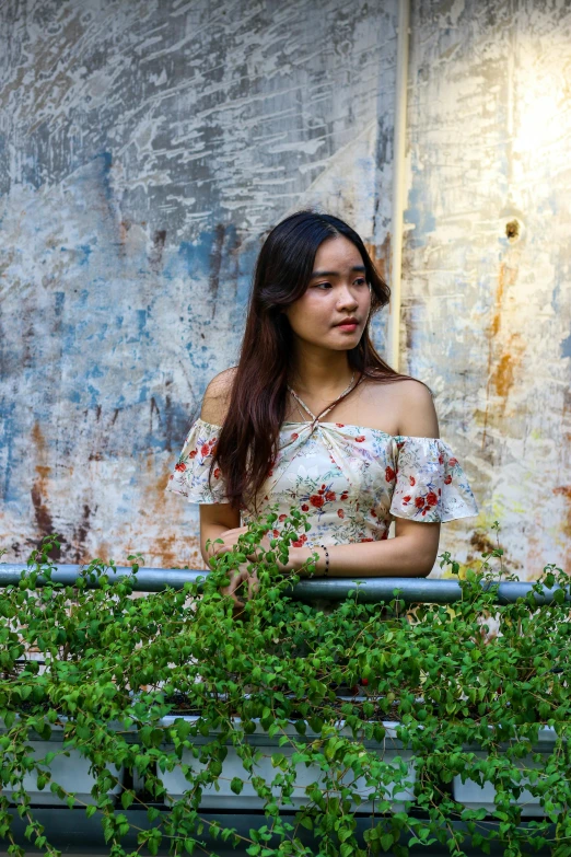 a woman standing by some green plants and a dirty wall