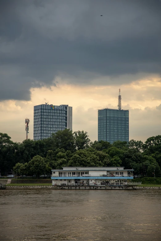 a small houseboat that's on the bank of a river, with tall buildings in the distance