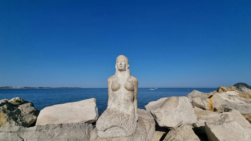 the statue is sitting near some rocks by the water