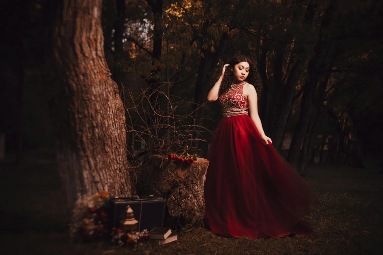 a young lady dressed in a red dress standing by a tree