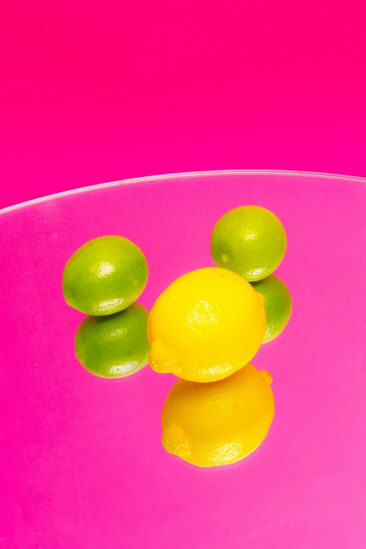 three limes and two lemons on pink background