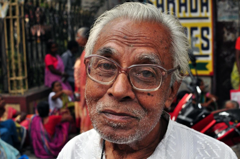 a man with white hair and glasses standing on street next to people