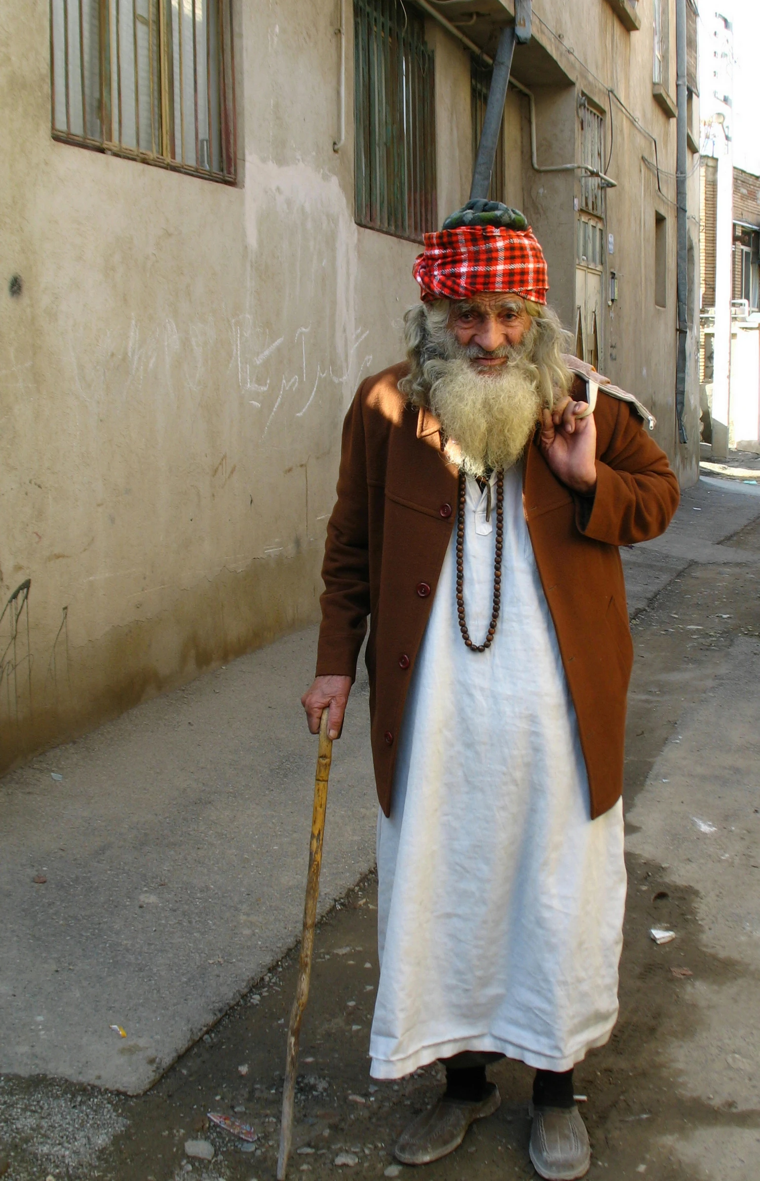 an older bearded person wearing a red and white hat and brown jacket