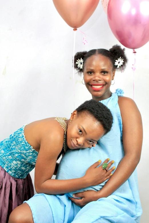 two women hug and smile while they pose in front of balloons