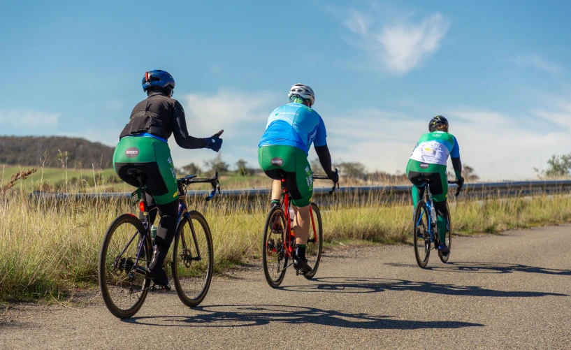 three cyclists on a rural road with grassy fields in the background