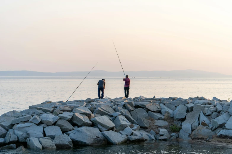 two men fishing on the edge of the rock wall