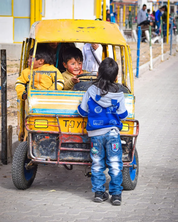 two small children ride in the back of a yellow pickup truck