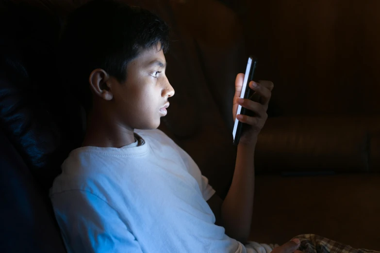 a boy sitting on the couch playing with his cell phone