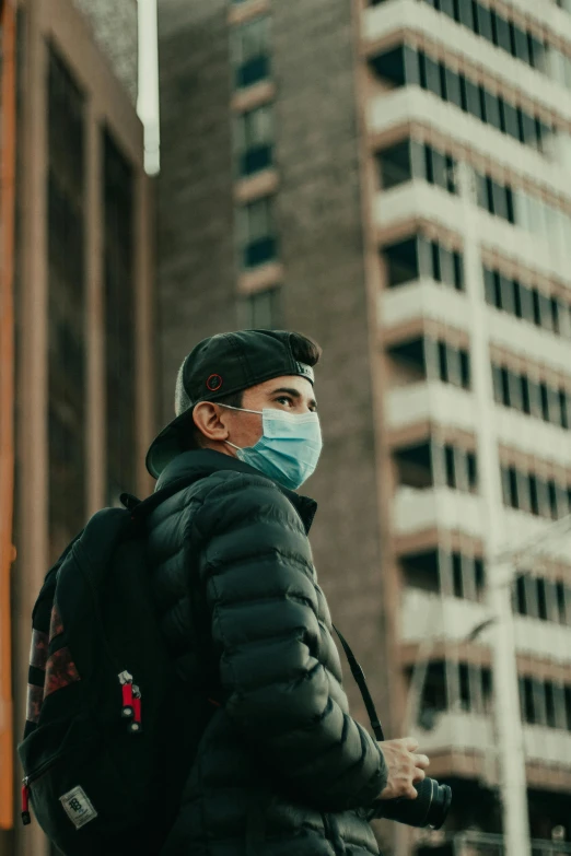 a man standing near a tall building wearing a face mask