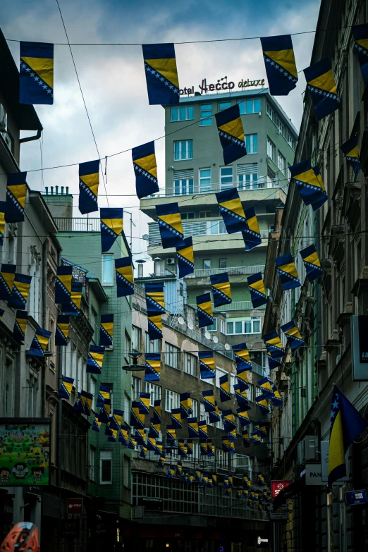 many flags are strung up in a row near tall buildings