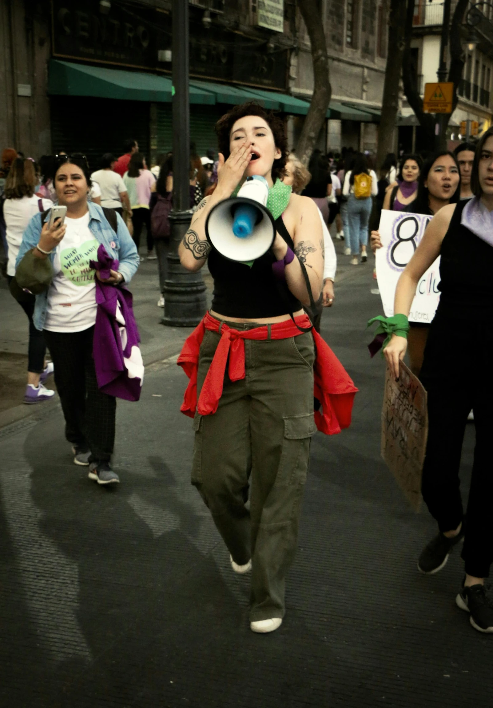 a lady wearing red and green clothing carrying a bullhorn in a street