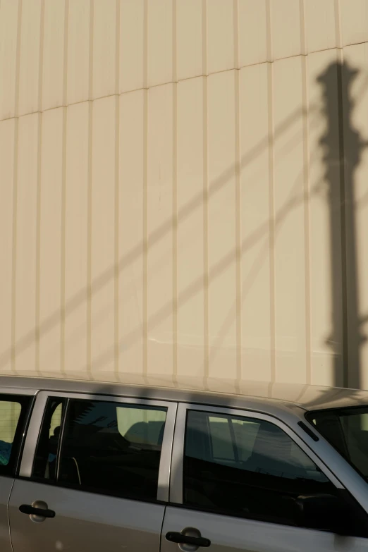 a grey car and a brown building are against a light pole