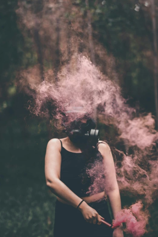 a young woman is standing in the woods, wearing a mask and smoking a pink stick