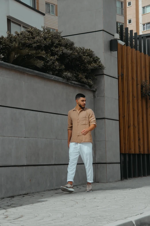 the man is standing in front of a building wearing a tan shirt and white pants
