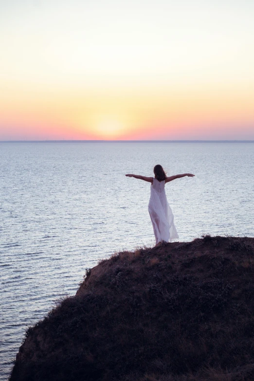 a woman with arms spread standing on a cliff near the ocean