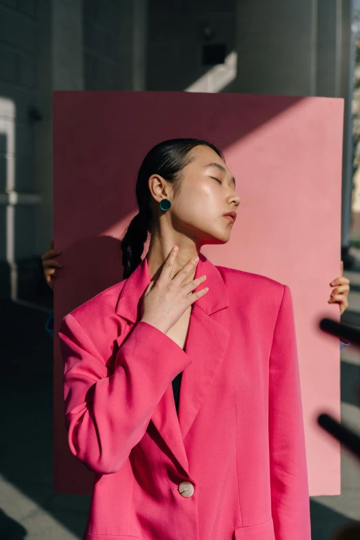 the model in a pink suit poses against a pink structure