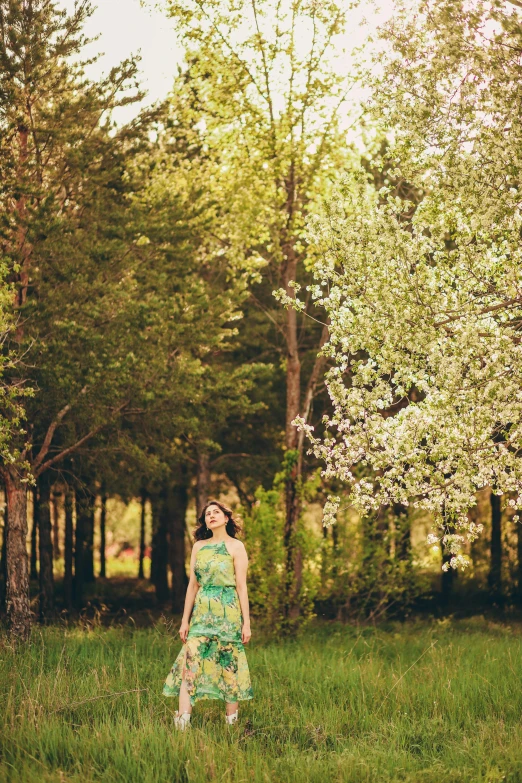 a girl standing in the grass by some trees