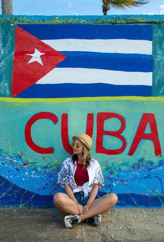 a person sitting on the sidewalk in front of a wall with the word cuba painted on it