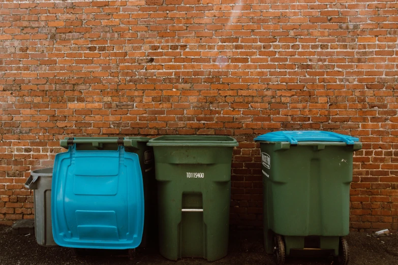 three trash cans sit against a brick wall