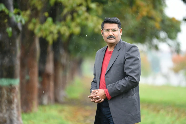 a man wearing a dark suit stands on the grass under some trees