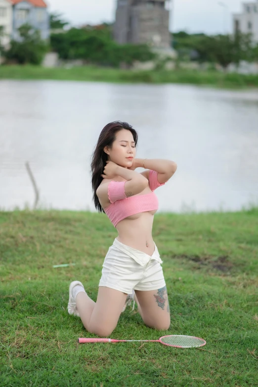 asian woman in the grass with a racket behind her