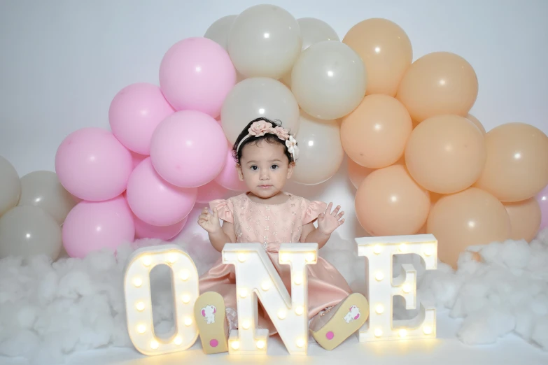 a baby girl sitting next to letters in front of balloons